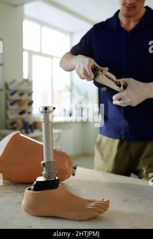 Operatore manuale in piedi davanti al luogo di lavoro con parti della protesi della gamba durante il controllo del lavoro del meccanismo dell'articolazione del ginocchio Foto Stock