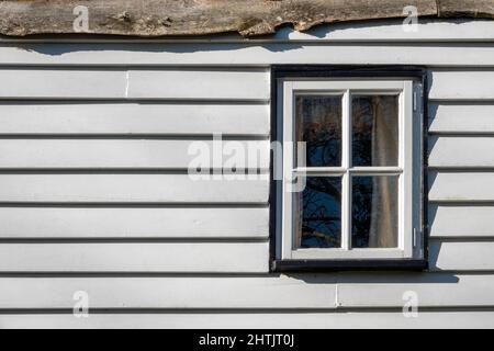 Una piccola finestra in legno dipinto di bianco a quattro sezioni posta in rivestimento di legno dipinto di bianco orizzontale, piatta su senza prospettiva Foto Stock