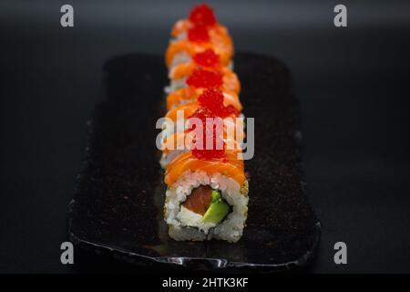 Californiano roll, giapponese Uramaki Sushi roll con salmone selvatico, avocado fresco, tobiko rosso e cremoso formaggio Philadelphia su sfondo nero. Foto Stock
