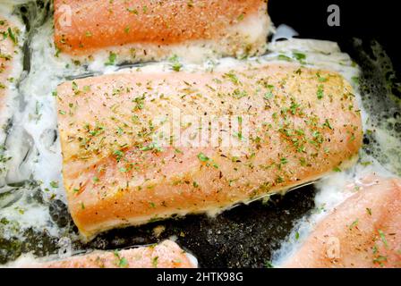 Salmoni in aglio, prezzemolo, pepe e burro in una padella Foto Stock