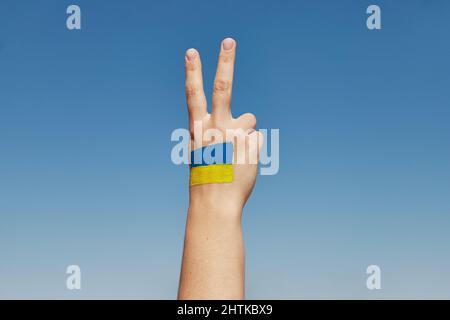 Womans mano con bandiera ucraino dipinto segno di pace contro il cielo blu. Fermare la guerra Foto Stock