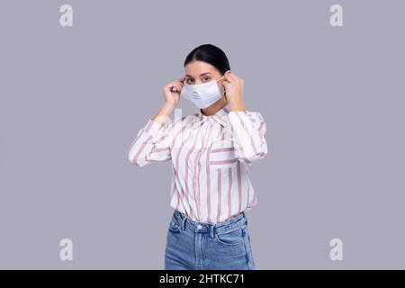 Ragazza mette su maschera medica isolato. Donna in camicia con maschera medica. Salute, virus, concetto medico Foto Stock