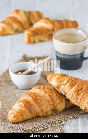 Deliziosi croissant francesi su un tavolo di legno bianco, una tazza di caffè e croissant sullo sfondo, scena della colazione, verticale Foto Stock
