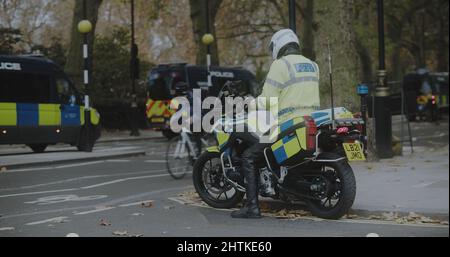 Londra, UK - 11 20 2021: Un ufficiale di polizia metropolitana su una moto pattugliando una strada laterale al largo di Millbank, furgoni di polizia seguire insulare la Gran Bretagna marzo. Foto Stock