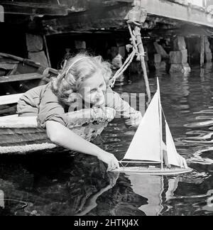 1940s estate. La giovane attrice Inga Landgré gioca con un modello di barca a vela in acqua in una giornata di sole. Svezia 1947 Kristoffersson Ref AC136-4 Foto Stock