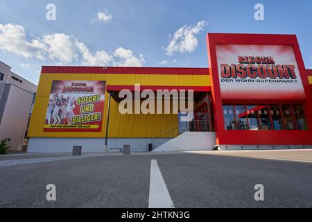 Germania - 21 maggio 2020: Rieger Sconto immediatamente ed economico, giallo rosso facciata con pubblicità, vetri riflettenti. Cielo blu nuvoloso Goeppingen. Foto Stock