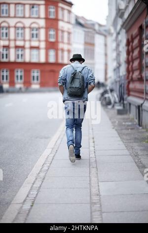 Sulla sua strada. Vista posteriore di un ragazzo che cammina lungo una strada della città. Foto Stock