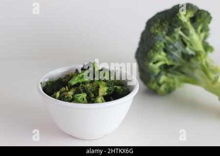 I broccoli saltati in un recipiente bianco, sparati su uno sfondo bianco insieme a un mazzetto di broccoli freschi Foto Stock