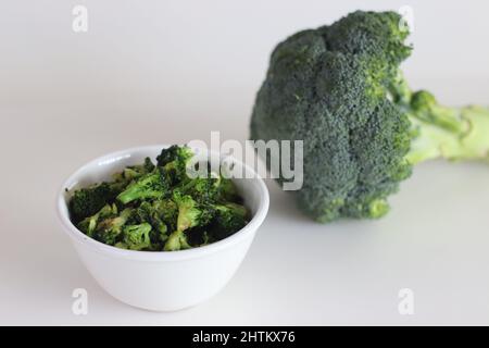 I broccoli saltati in un recipiente bianco, sparati su uno sfondo bianco insieme a un mazzetto di broccoli freschi Foto Stock