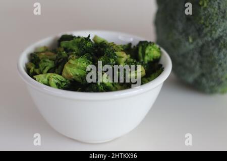 I broccoli saltati in un recipiente bianco, sparati su uno sfondo bianco insieme a un mazzetto di broccoli freschi Foto Stock