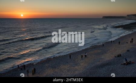 Le persone si riuniscono sulla spiaggia a Birling Gap vicino alle scogliere di Seven Sisters nel Sussex orientale, Regno Unito, per guardare il tramonto. Foto Stock