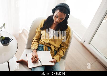 Senza musica, il mondo sarebbe un luogo noioso. Scatto ad angolo alto di una giovane donna d'affari attraente seduta nel suo salotto e scrivere note Foto Stock