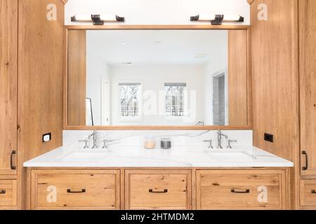 Un grande armadietto in legno in un lussuoso bagno con ripiani in marmo e due lavandini. Foto Stock