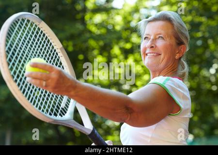 Preparazione al servizio - tecnica di tennis. Donna anziana che si prepara a servire una palla da tennis. Foto Stock