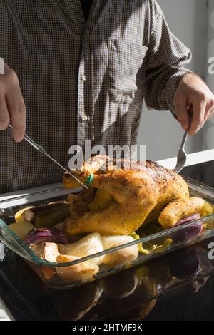 Uomo irriconoscibile che prepara un succosa pollo al forno con verdure. Cucina soleggiata. Foto Stock