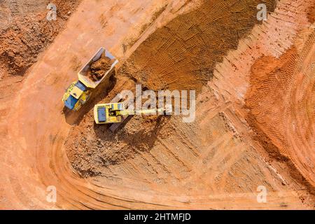 Il bulldozer sta raschiando uno strato di terreno e l'escavatore sta scavando e scaricando terra per il carico sul dumper Foto Stock