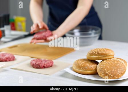 Mano della donna che forma una carne di manzo per una festa di hamburger. Porzionamento carne macinata. Hamburger fatti in casa. Fare il cibo a casa. Foto Stock