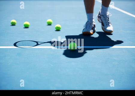 La pratica rende perfetto. Colpo di un uomo non identificato uomo in piedi su un campo da tennis. Foto Stock