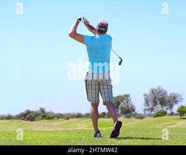 Puntando verso il verde. Vista posteriore di un golfer maschio maturo che gioca un colpo. Foto Stock