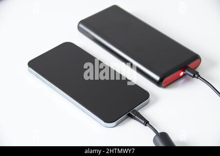 Il telefono si sta caricando dal powerbank su un tavolo bianco. Foto Stock