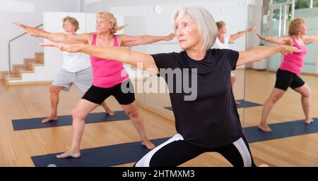 Donna anziana in piedi in affondo asana Virabhadrasana in studio yoga Foto Stock