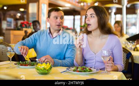 Una coppia positiva mangia insalata e beve vino al ristorante Foto Stock