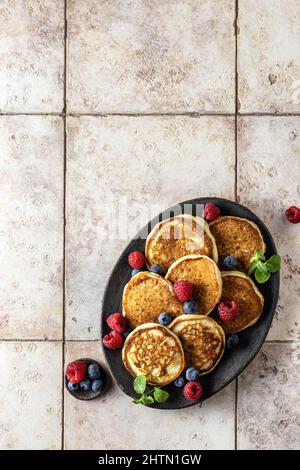 Pancake in piastra di ceramica marrone con foglie di mirtillo, lampone e menta, vista dall'alto Foto Stock