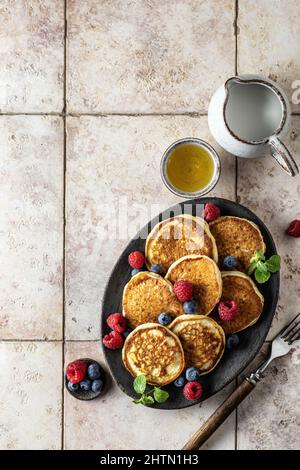 Pancake in piastra di ceramica con frutti di bosco, foglie di menta, miele e forchette, vista dall'alto Foto Stock