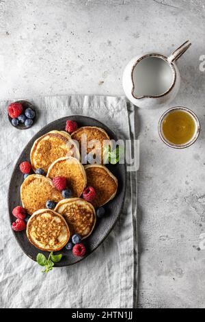 Pancake in piastra di ceramica con frutti di bosco, foglie di menta, barche con sugo di carne su tovagliolo di lino, vista dall'alto Foto Stock