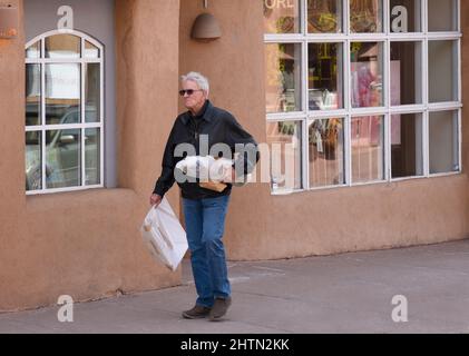 Un turista che visita Santa Fe, New Mexico, cammina lungo un marciapiede con i suoi acquisti da una galleria d'arte. Foto Stock