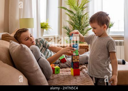 Divertenti ragazzi maschi che costruiscono la torre da diversi cubi di Rubik giocando insieme sul divano a casa Foto Stock