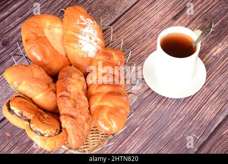 Un cestino con un assortimento di dolci fatti in casa e una tazza di tè nero caldo su un tavolo di legno. Primo piano. Foto Stock