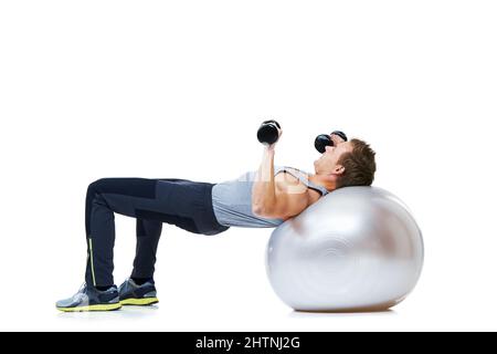 Tenendosi tondo. Colpo di un uomo che si bilancia su una sfera di esercizio che solleva pesi. Foto Stock