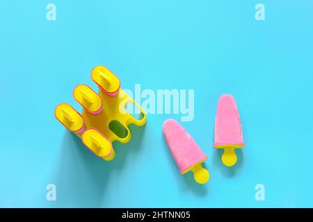 Popsicles fatti in casa. Gelato alla fragola naturale in stampi di plastica su sfondo blu con spazio copia. Vista dall'alto modello di disposizione piatta per il. Foto Stock