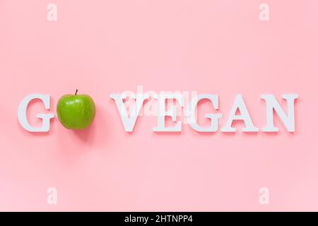 Andare vegan dieta sana concetto. Verde naturale mela fresca in parola Vai Vegan da lettere bianche su sfondo rosa. Creative Flat Lay Top View spazio di copia Foto Stock