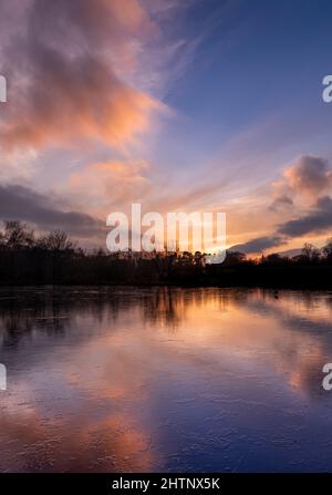 Tramonto sul cielo colorato su un lago ghiacciato. Bulwell Hall Park Nottingham Inghilterra Regno Unito Foto Stock