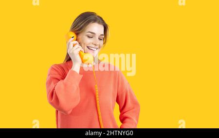 Donna sorridente con cornetta retrò in mano isolata su sfondo giallo brillante. Foto Stock