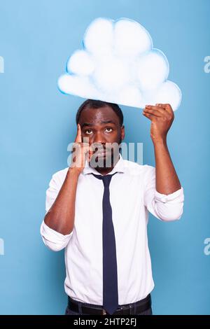 Ritratto di un uomo d'affari professionista che punta al white paper idea cloud in piedi di fronte a sfondo blu. L'imprenditore afro-americano pensa sotto la bolla del pensiero. Foto Stock