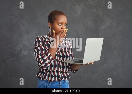 Emotiva donna con pelle scura e sconcertata espressione guarda il laptop nelle sue mani. Foto Stock