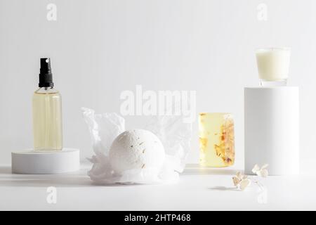 bomba da bagno, sapone fatto a mano, olio e candela sul podio su sfondo bianco. Natura morta, relax, concetto di benessere. Composizione per salone spa. Spazio copia Foto Stock