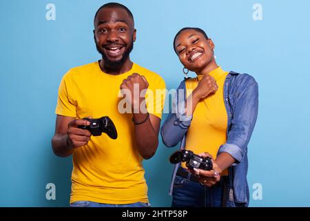 Fidanzato allegro e ragazza che gioca video giochi per vincere. Coppia felice usando il controller per giocare online e vincere l'azione di gioco sulla console. Persone che tengono il joystick su Buon divertimento. Foto Stock