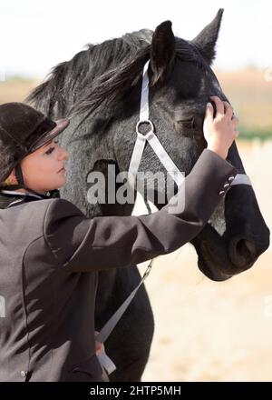 Prepararsi per una lunga corsa. Shot di una giovane femmina che stroking il suo viso cavalli. Foto Stock