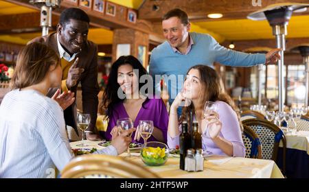 Uomini che chiacchierano con un gruppo di donne nel ristorante Foto Stock