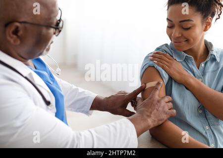 Donna nera che viene vaccinata contro Covid, Dottore che applica Plaster Foto Stock