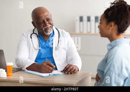 Medico di sesso maschile consulenza giovane donna incinta sorridente, scrittura record Foto Stock