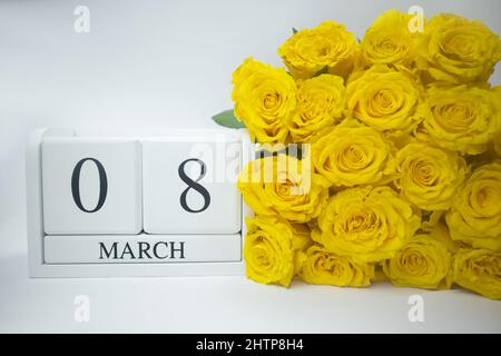 Calendario in legno Marzo 8 e rose gialle su sfondo bianco. Foto Stock