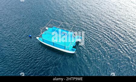 Foto con drone dall'alto verso il basso di un piccolo catamarano ancorato su un mare blu profondo. Un piccolo catamarano blu in mare aperto Foto Stock