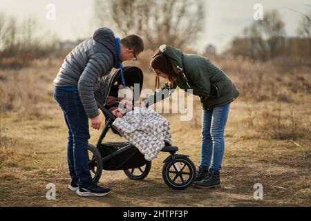 Famiglia giovane con la loro bambina che cammina attraverso il parco con carrozzina in una zona residenziale Foto Stock