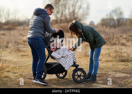 Famiglia giovane con la loro bambina che cammina attraverso il parco con carrozzina in una zona residenziale Foto Stock