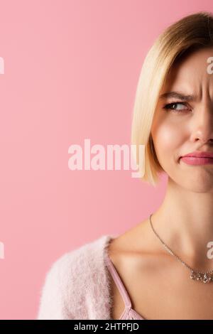 vista ritagliata della giovane donna incerta accigliata e guardando via isolato su rosa, immagine di stock Foto Stock